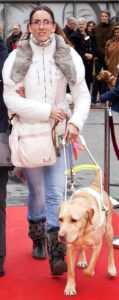 Foto van Debby die met blindengeleidehond Tobias over de rode loper van de Dogwalk loopt tijdens Complimentendag 2013. Deze middag werd georganiseerd door KNGF Geleidehonden in het centrum van Amstelveen. Tobias is een blonde labrador.