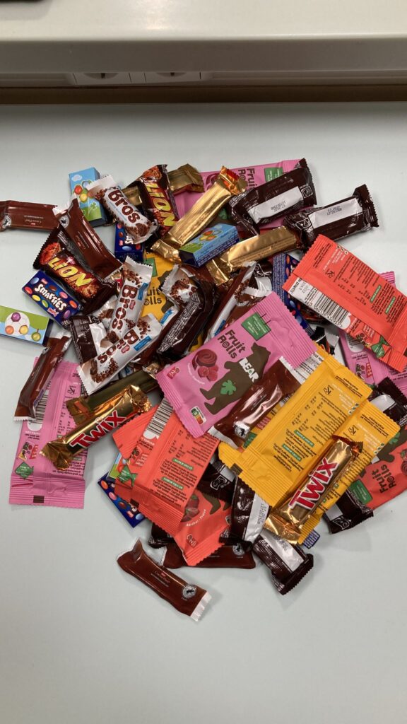 Foto van een berg snoepgoed op een tafel. Er liggen o.a. Marsjes, Twixjes, Brosjes, Bounty’s, doosjes met Smarties en pakjes gedroogd fruit.