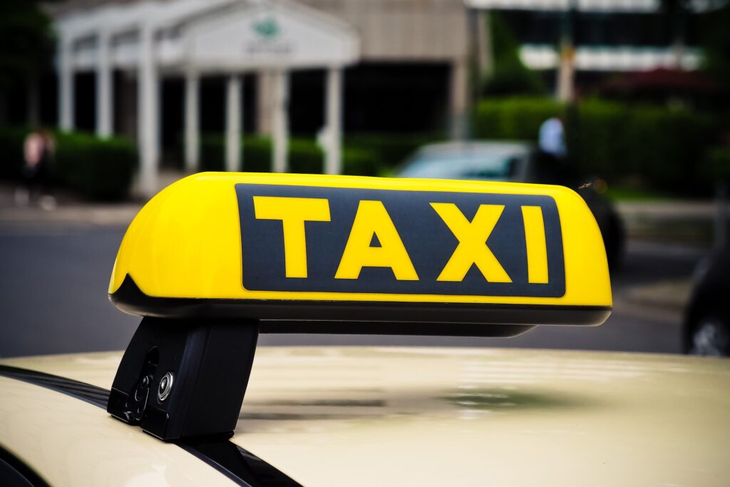 Foto van het dak van een taxi met een bordje met het woord ‘Taxi’ erop.