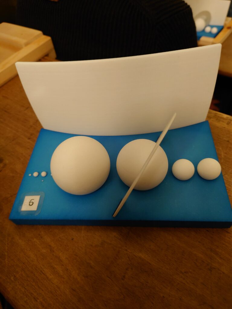 Foto van een model met acht grote en kleine bolletjes, die symbool staan voor de planeten in ons zonnestelsel. Het doel van het model is om te laten zien hoe groot de planeten zijn en om zo te voelen dat bijvoorbeeld de aarde veel kleiner is dan Jupiter.