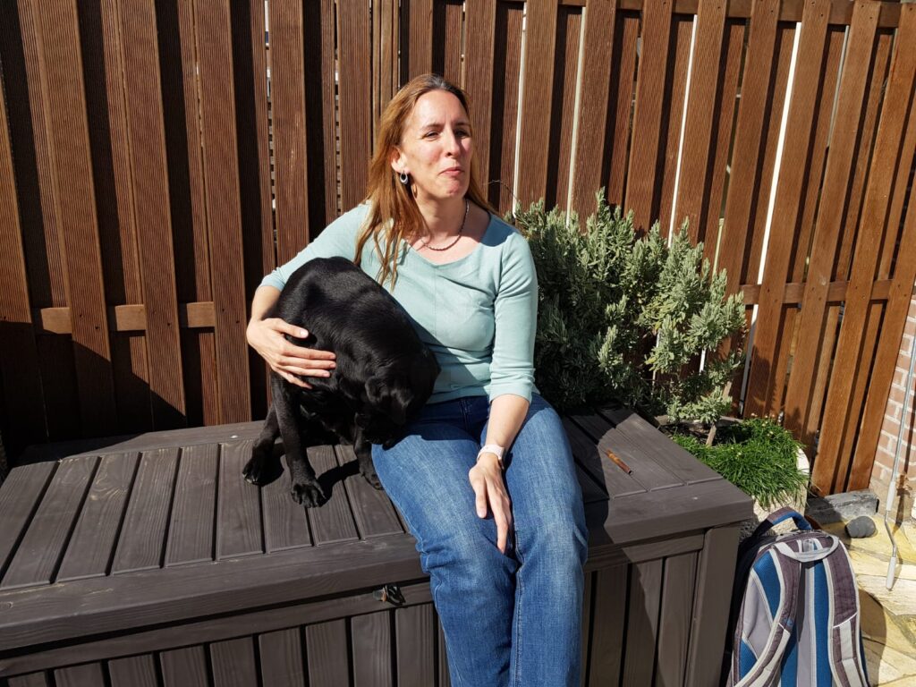 Zwarte labrador Tarka zit naast Debby op een kist in de tuin