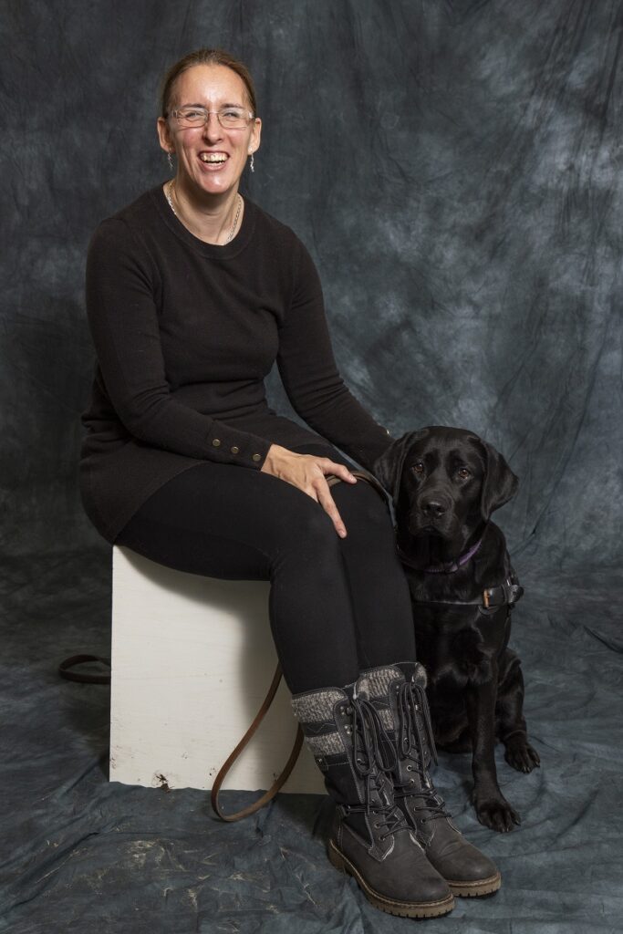 Foto van zwarte labrador Tarka, die naast Debby op een verhoging zit.