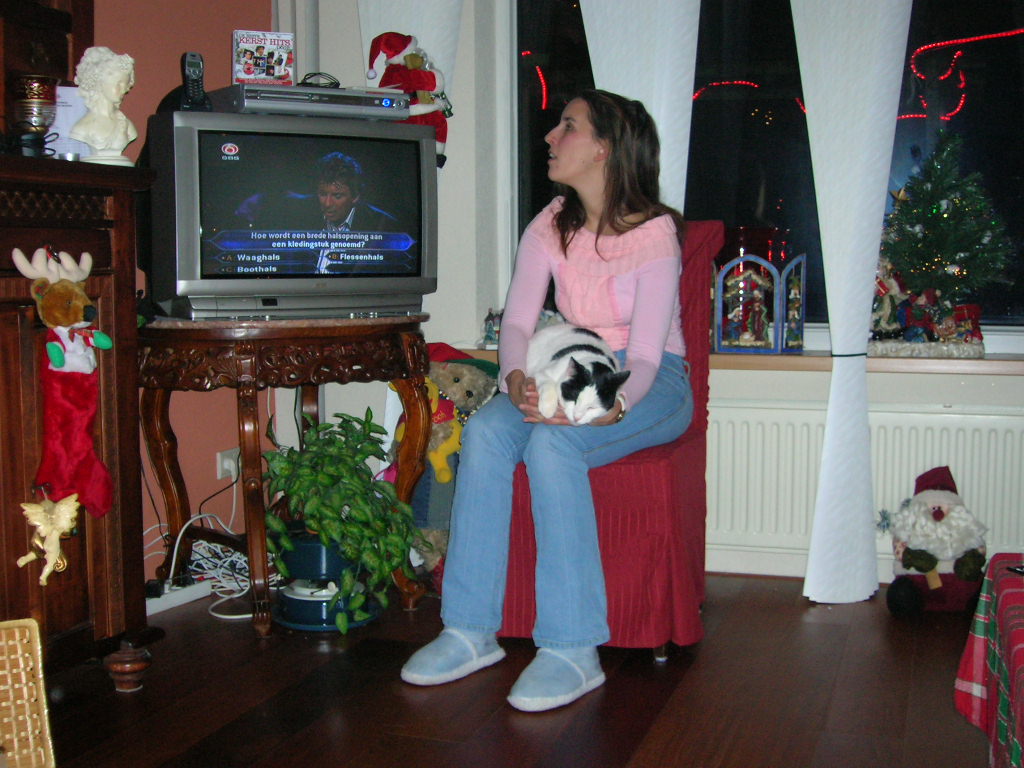 Foto van Debby (ongeveer 26 jaar) die bij haar ouders thuis vlak voor de tv zit met wit-zwarte kat Goofy op schoot.