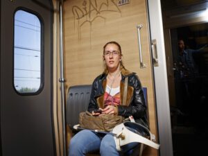 Foto van Debby die op een bankje in een trein zit met blonde labrador Tobias onder de bank.