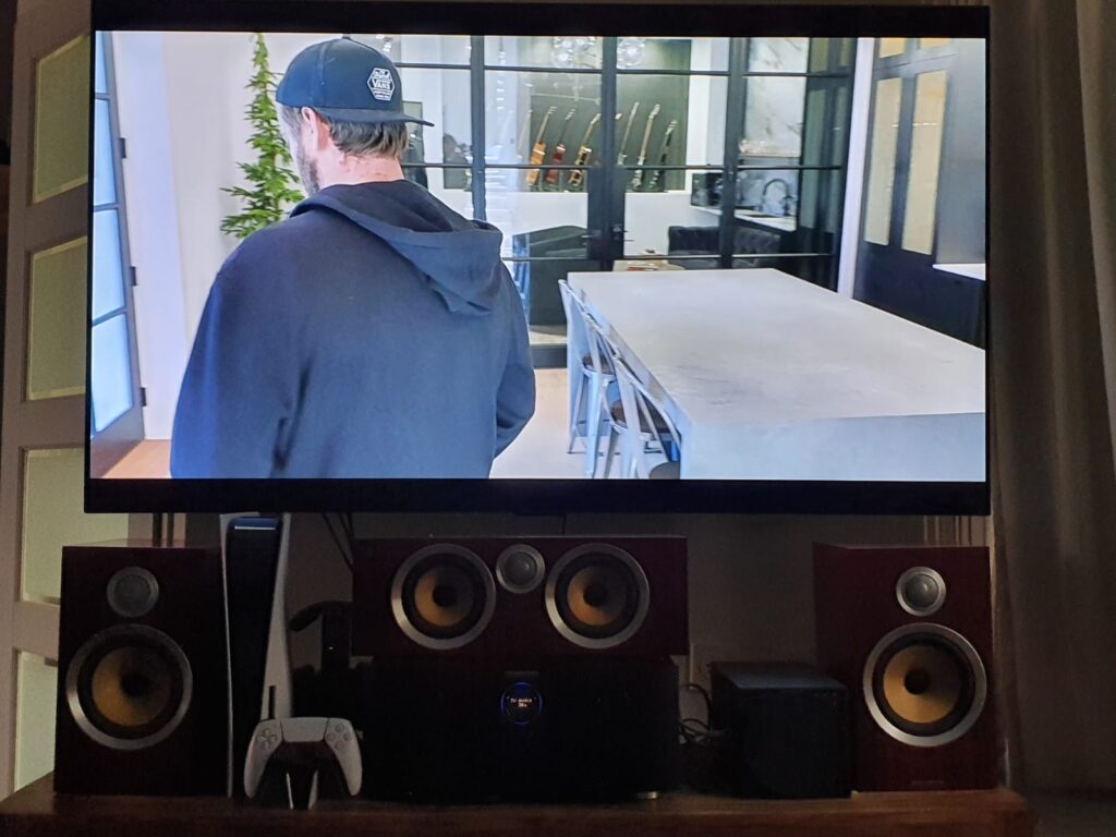 Foto van een grote tv met daaronder op een tv-kasje boksen en een receiver.