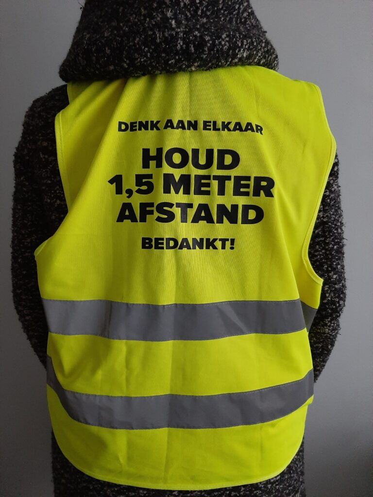 Foto van de achterkant van een groen hesje met de vraag 1,5 meter afstand te houden.