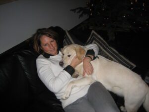 Zeer blonde labrador pup, Umbar, zit met zijn poten op schoot bij zijn tweede pleegbazin.